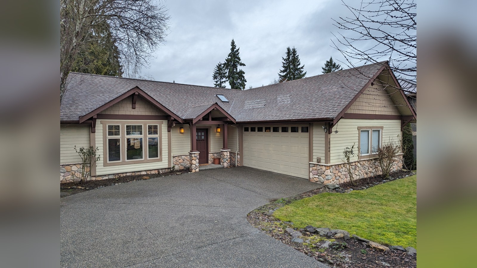 Photo: a tan one-story house with stone trim, a two-car garage and a wide driveway.