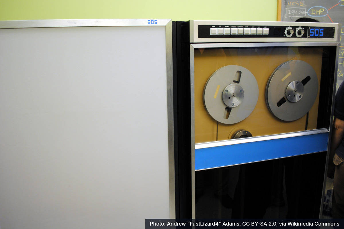 Photo: an SDS Sigma 7 mainframe computer with two tape reels behind a glass panel, in the restored UCLA lab.