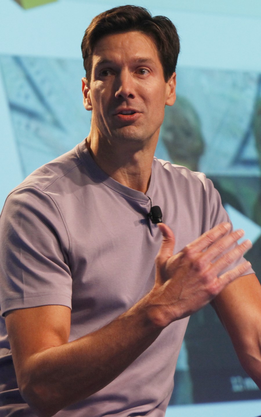 Photo: Mark Russinovich, a man in a gray-purple T-shirt with a small clip-on microphone, mid-sentence on a stage with one hand raised.
