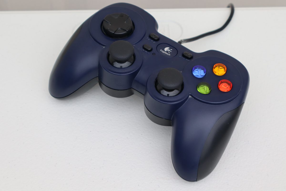 A navy-blue wired Logitech F310 gamepad with a black D-pad, two black thumbsticks and blue, green, red and orange face buttons, on a white surface.