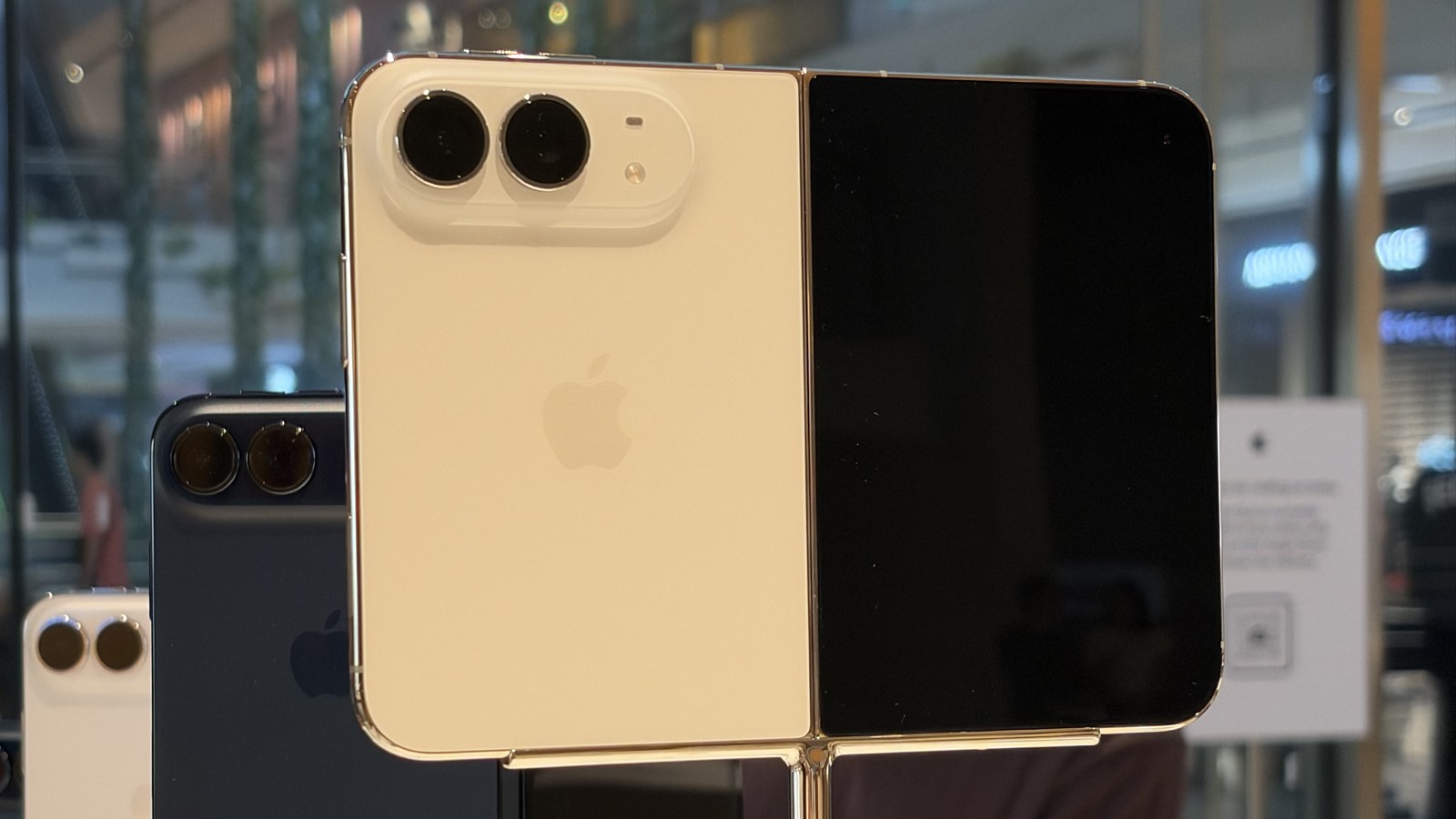 An open iPhone Duo with a light-colored back and two rear cameras on a store display stand, with more iPhone Duo phones behind it.