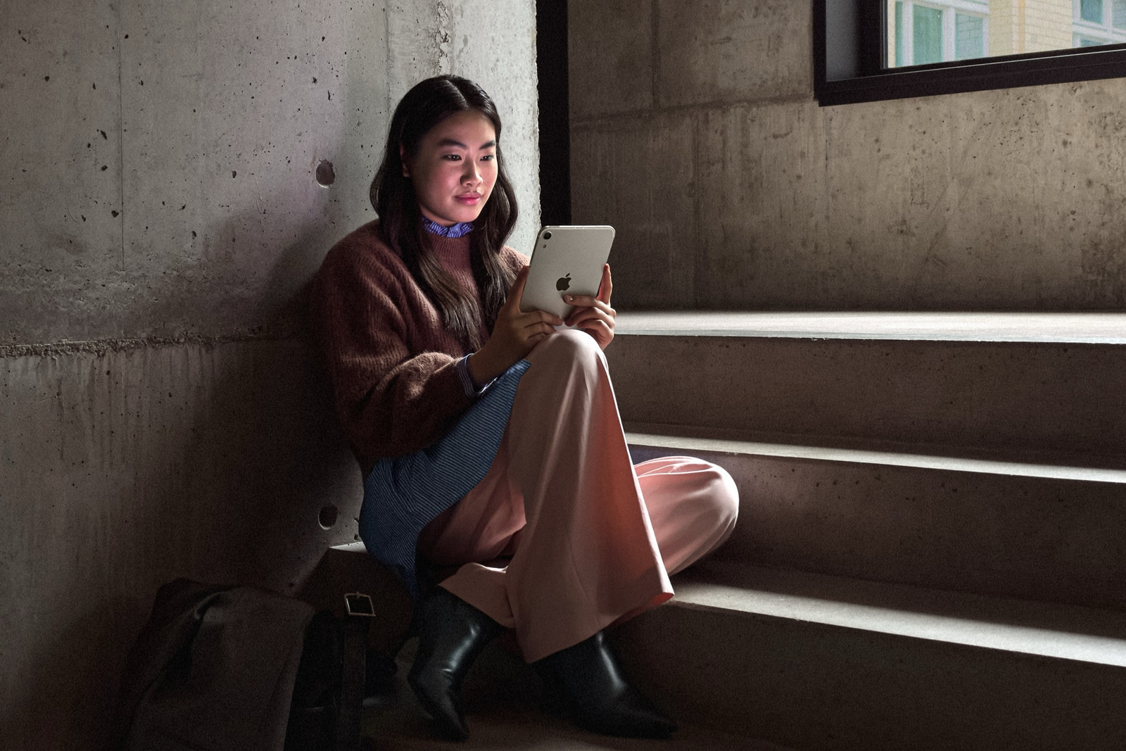 Photo: A woman sits on concrete steps and looks at Apple's new iPad mini.
