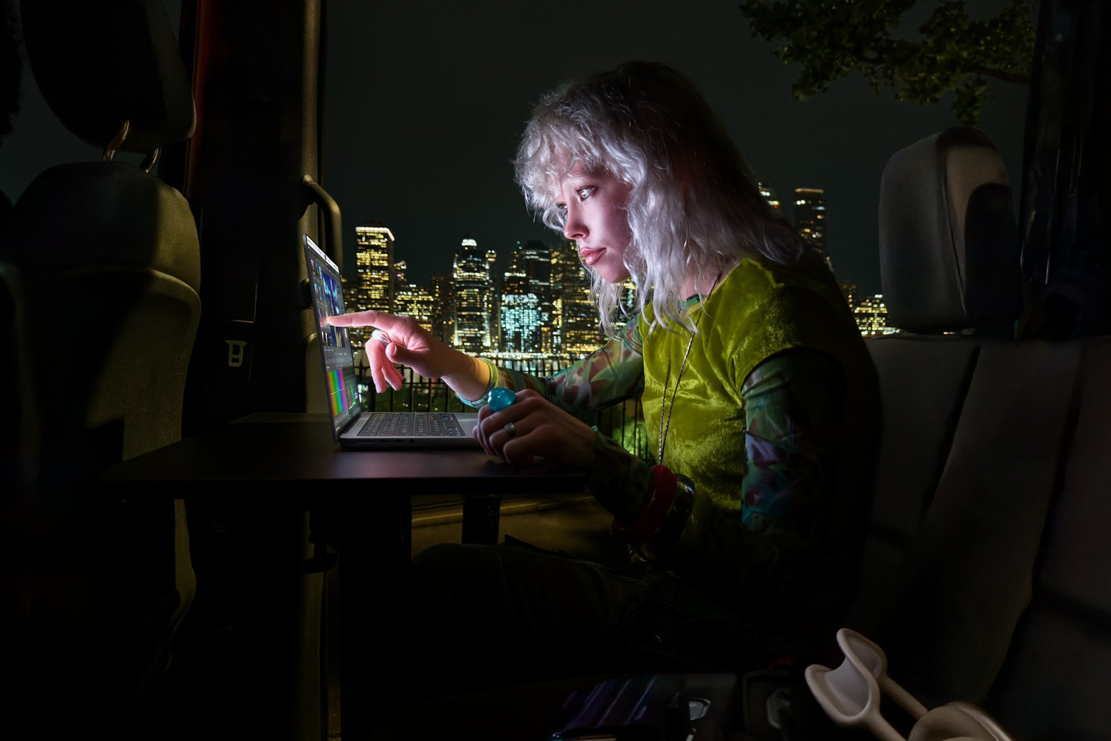 Photo: A woman in a van at night touches the new MacBook Pro's screen, with a city skyline behind her.