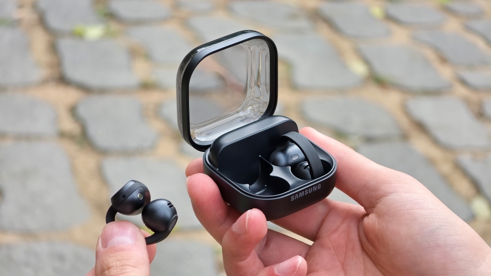 A hand holding the open Galaxy Buds On charging case with one earbud pinched between two fingers